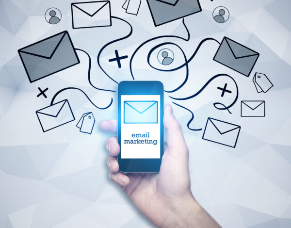 Hand holding smartphone with abstract email network hologram on polygonal wall background. E-mail marketing concept